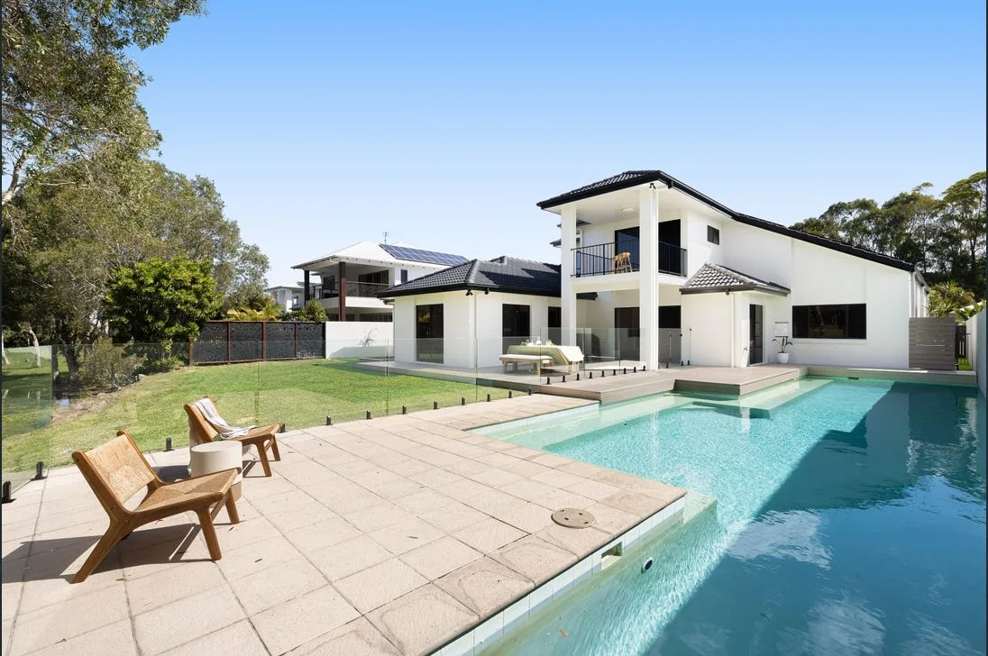 A modern white two-storey Brisbane home with a frameless glass pool fence