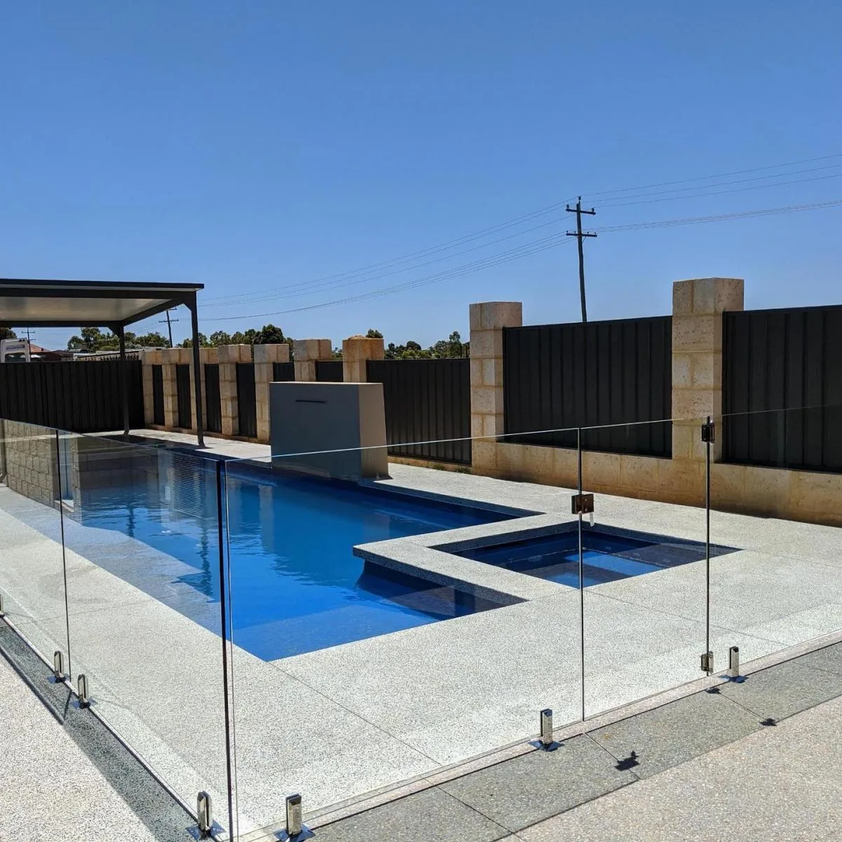 A frameless glass pool fence around a pool and spa with a waterfall feature