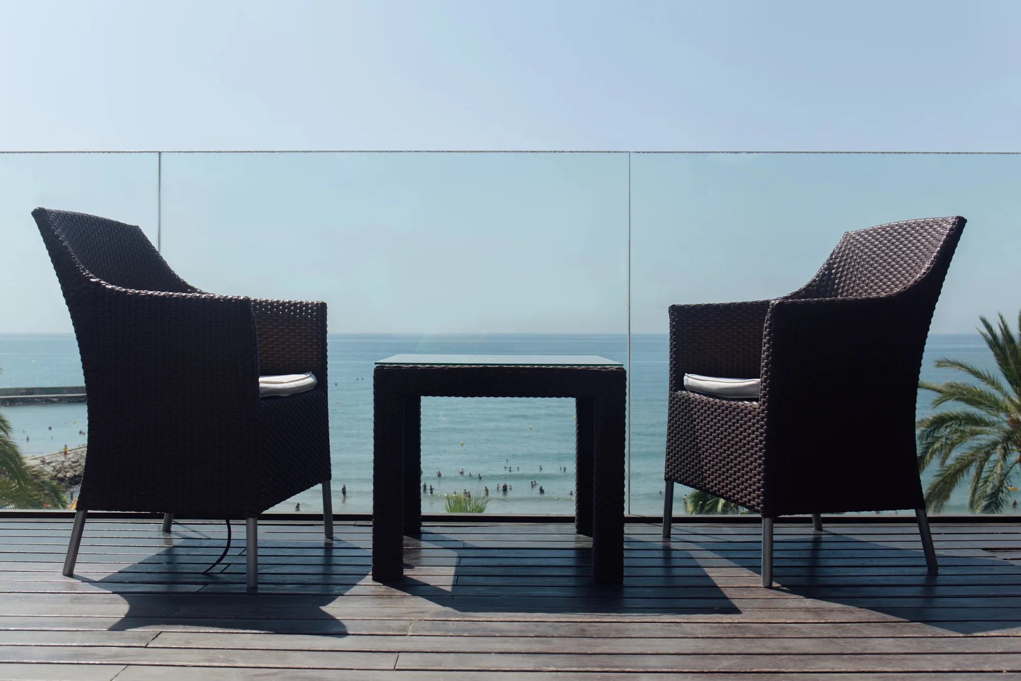 Outdoor furniture beside a frameless glass balcony balustrade with an ocean view