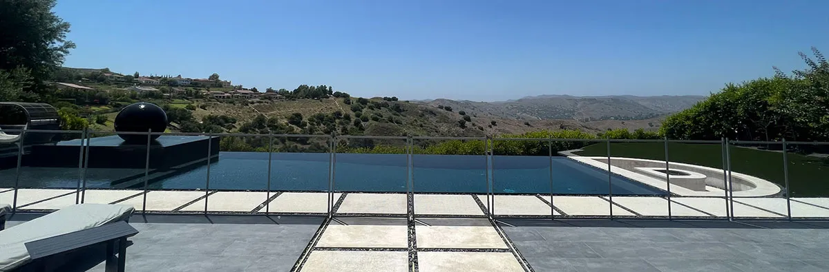 A frameless glass pool fence around an infinity pool on a hillside property