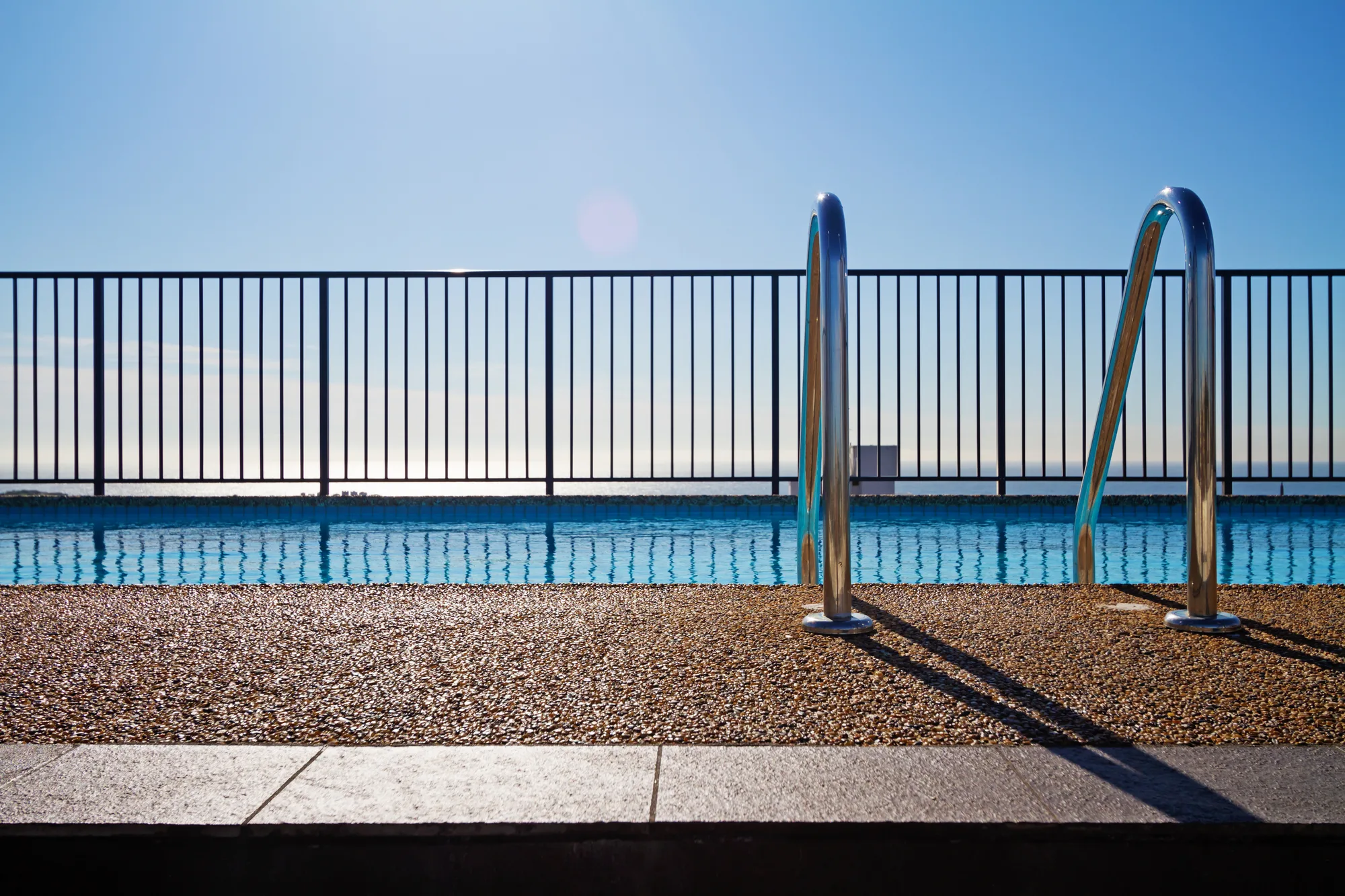 Black tubular pool fencing beside pebble pool decking